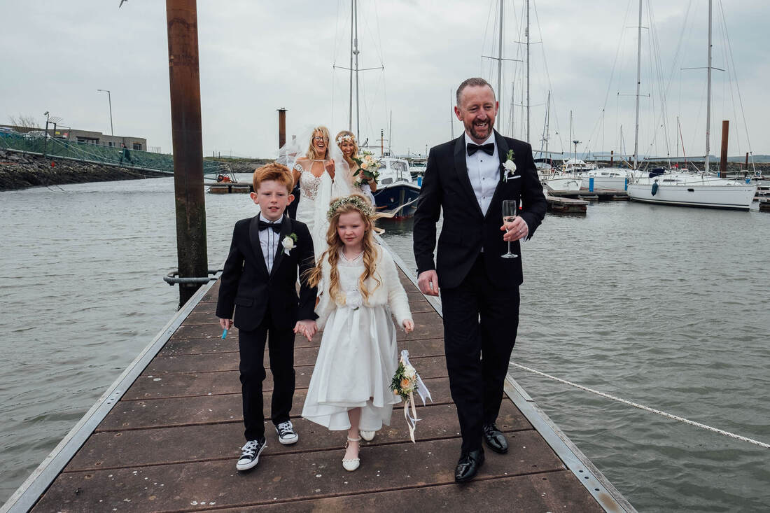 A candid wedding photograph of Des, Laura & Family stop at Fahan Marina on their Wedding Day while travelling between their wedding service at St Patrick's Chapel, Derry, Northern Ireland and their reception at The Inishowen Gateway Hotel, Buncrana, County Donegal