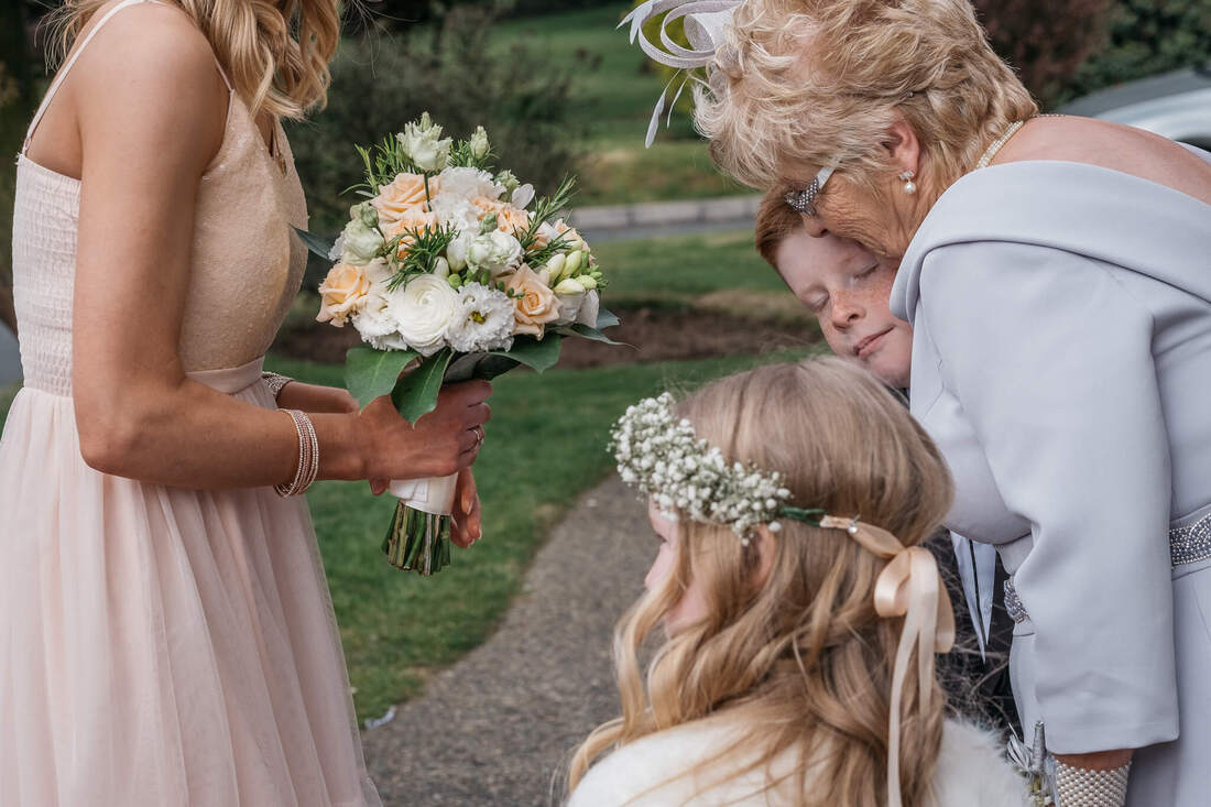 Granny hugging the pageboy at a Derry wedding while a bridesmaid & flowergirl look on