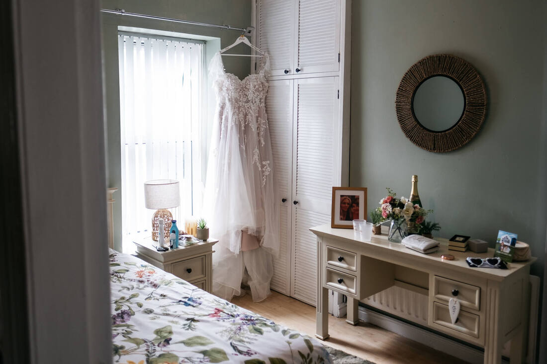 A wedding dress hangs from a curtain rail in the corner of the brides bedroom