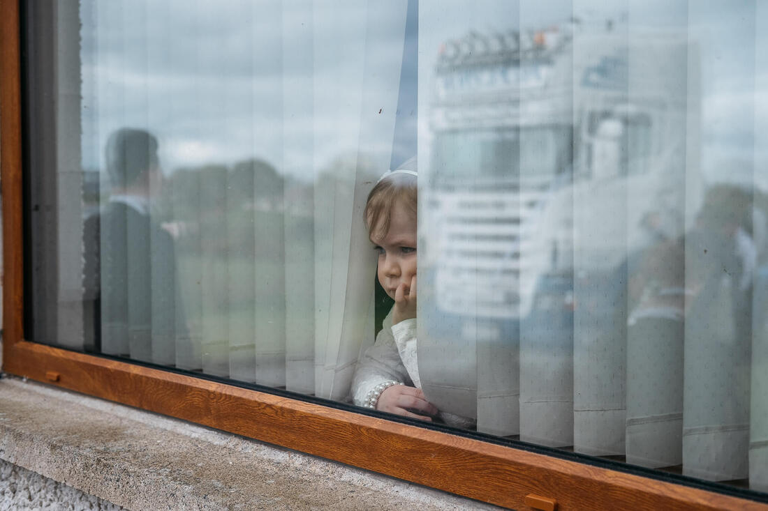 A young girl forlornly looks on as the groom & goomsmen head off to the wedding in a truck - which is reflected in the window the girl is looking through 
