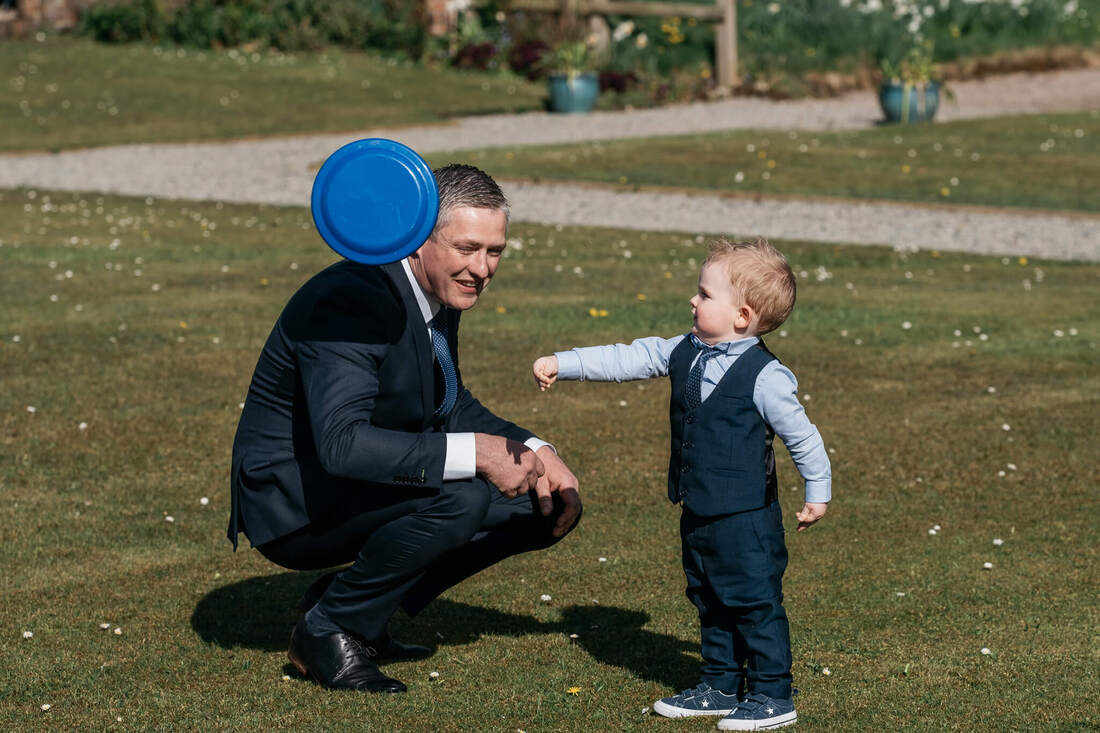 A young wedding guest throwing a frisbee which is passing by his dad's head