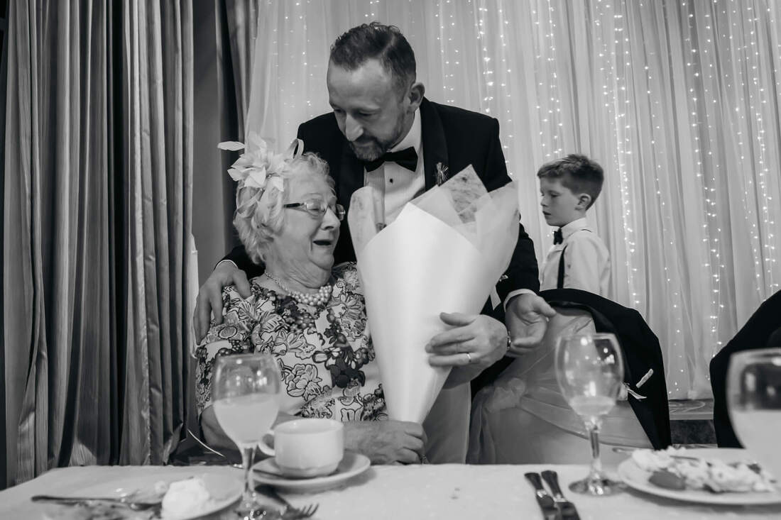 The groom hugs his smiling mum while presenter with with a bouquet of flowers
