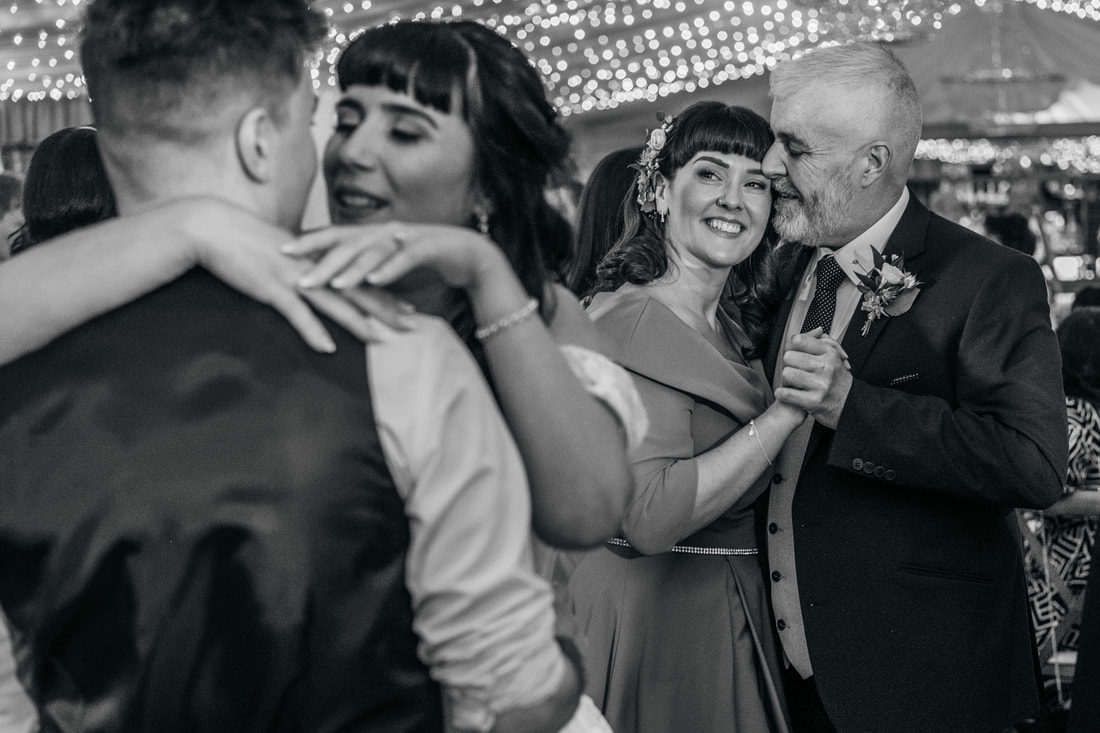 The bride and groom enjoy their first dance while the father and mother of the bride watch on lovingly