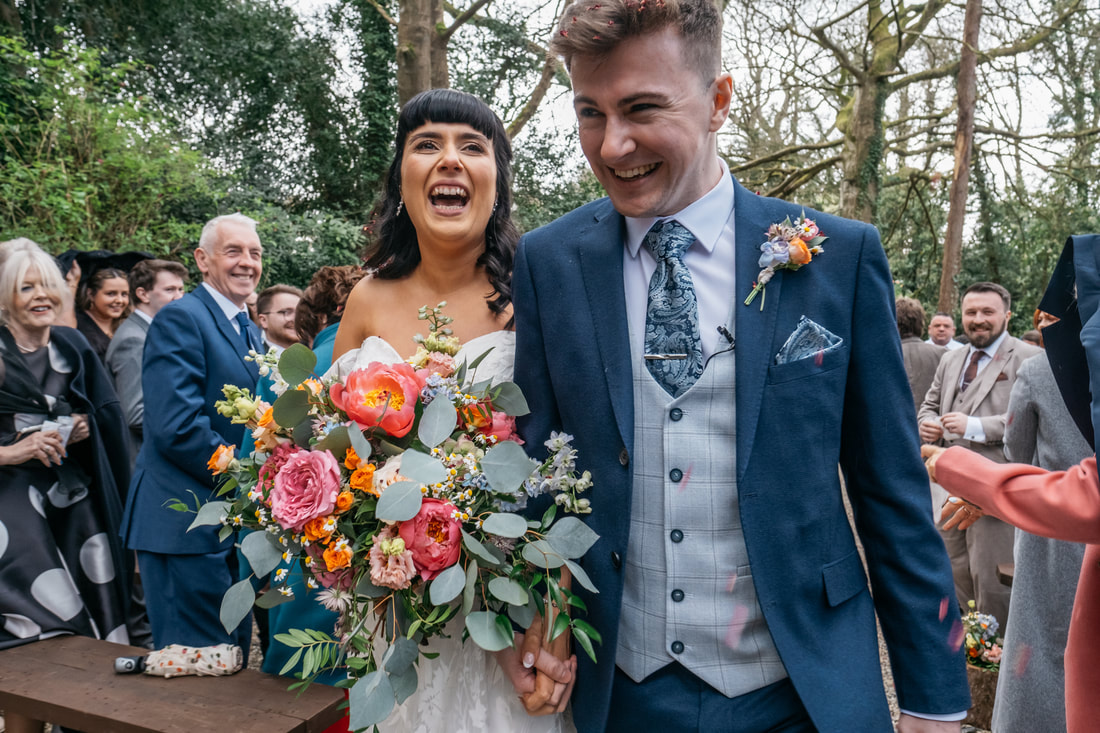 The joyful faces of a bride and groom as they are showered in confetti while leaving their forest wedding ceremony