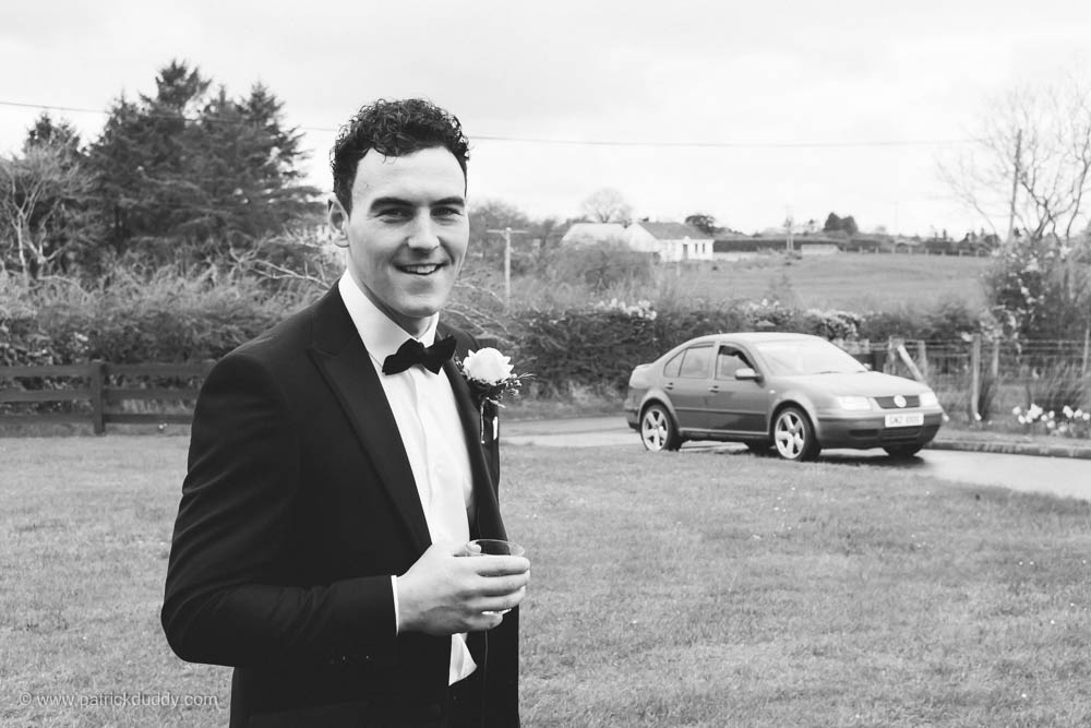 Groomsman in a tuxedo with a drink waits for the wedding cars to travel to Ballyscullion Park Wedding by Patrick Duddy Wedding Photography