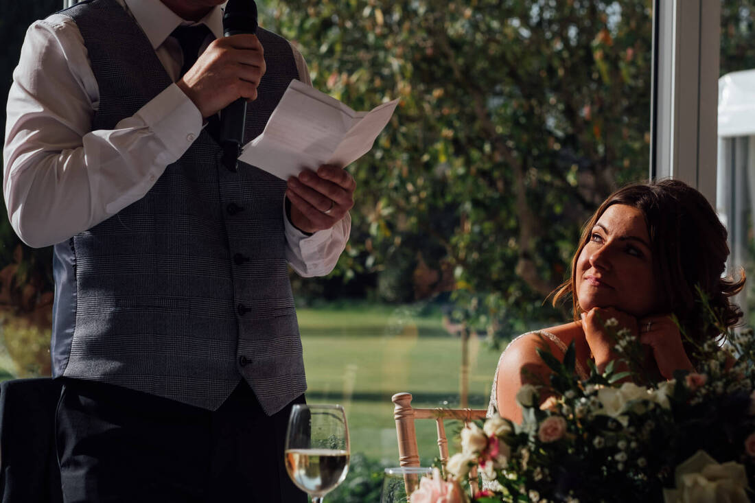 A Candid Photograph of Bride, Maria, watching Groom, Kevin, Make His Wedding Speech at Ballyscullion Park, Derry, Ireland by Patrick Duddy Documentary Wedding Photography
