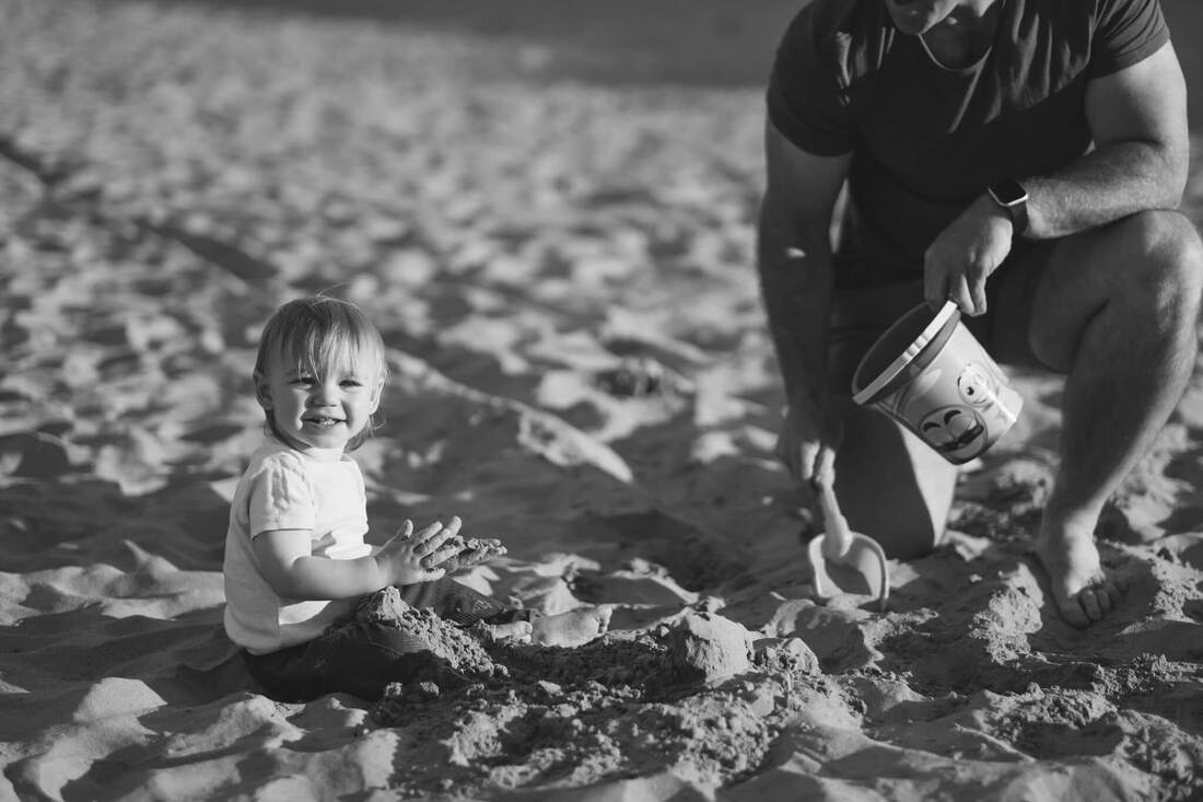 A baby on the beach - a black and white image of a child on a beach playing while his father watches on