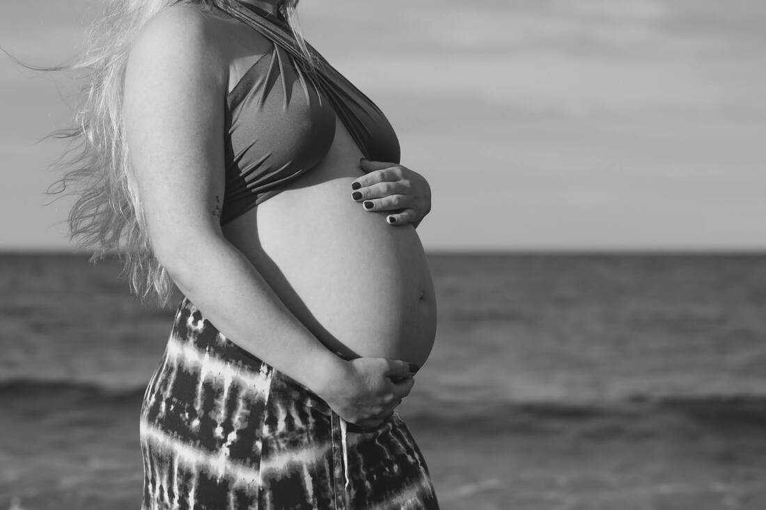 A black and white portrait of a baby bump on a beach