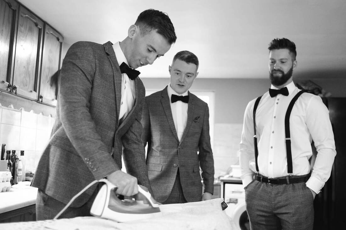 A candid shot of one groomsman ironing the others jacket, while the groom watches nervously one