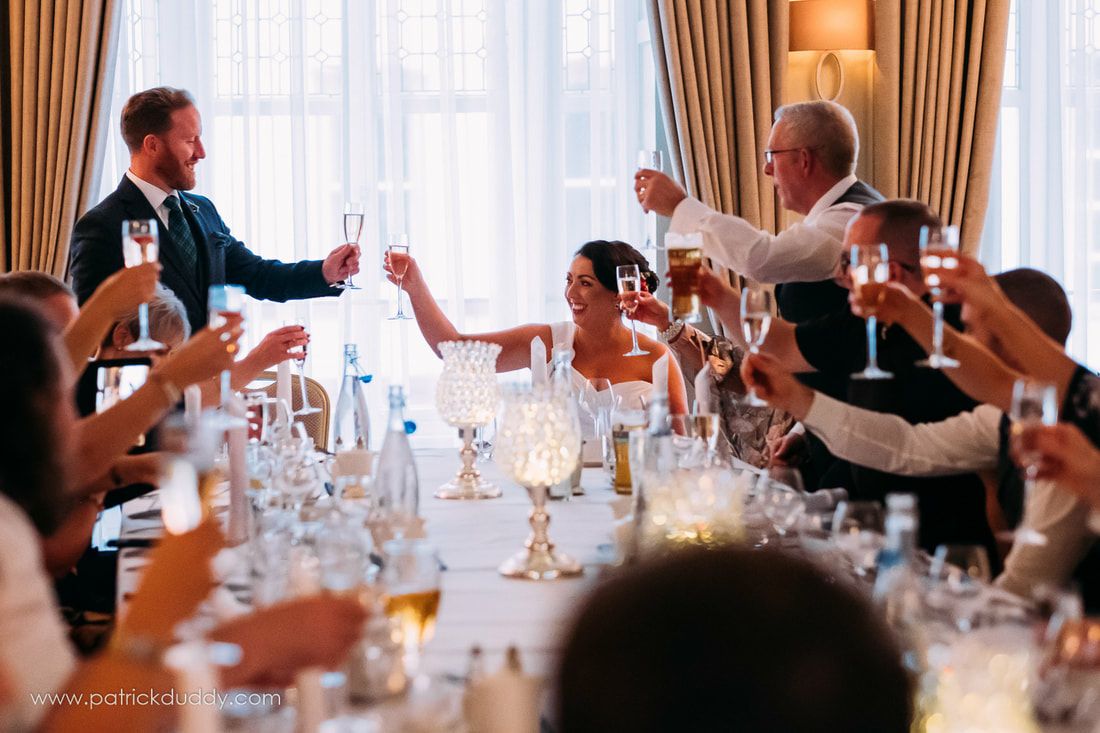 A candid photograph as family and friends raise a glass to the bride and groom in Bishops Gate Hotel, Derry, Ireland
