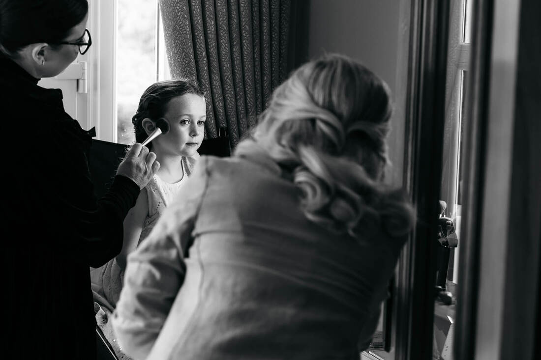 A young family member takes her turn in the make up artists chair at the grooms house on the wedding day