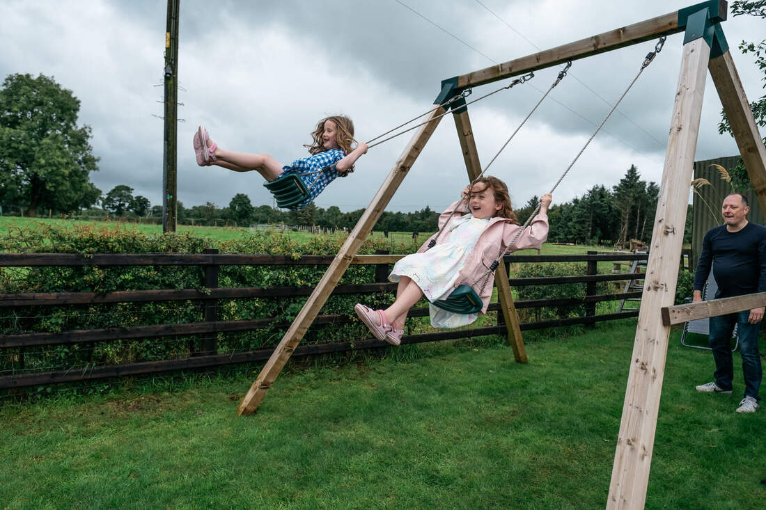 Young wedding guests having a go on the swings in the grooms garden before getting ready for the day ahead