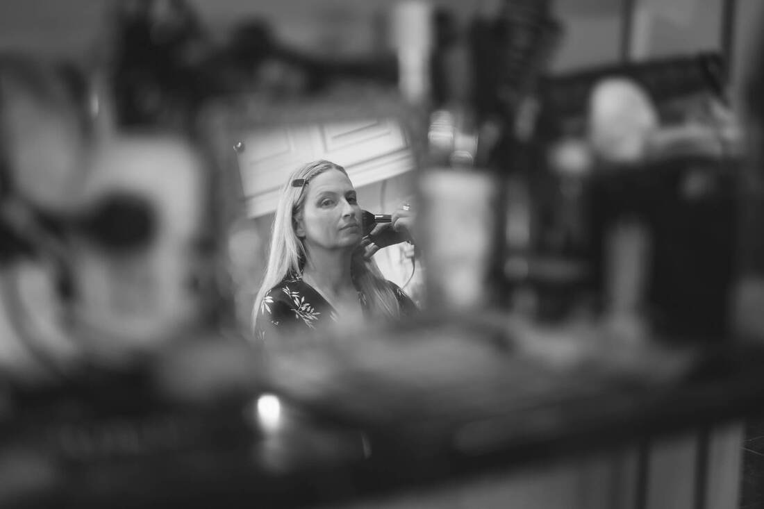 A black and white photograph of a bride's reflection in a mirror as she sits for the make up artist on the morning of her wedding in Donegal