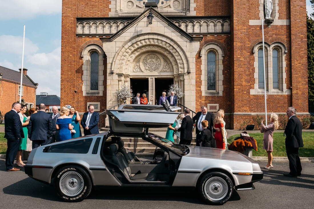 A photograph of the De Lorean car from back to the future parked outside St Patricks Chapel Pennyburn as guests arrive prior to the wedding