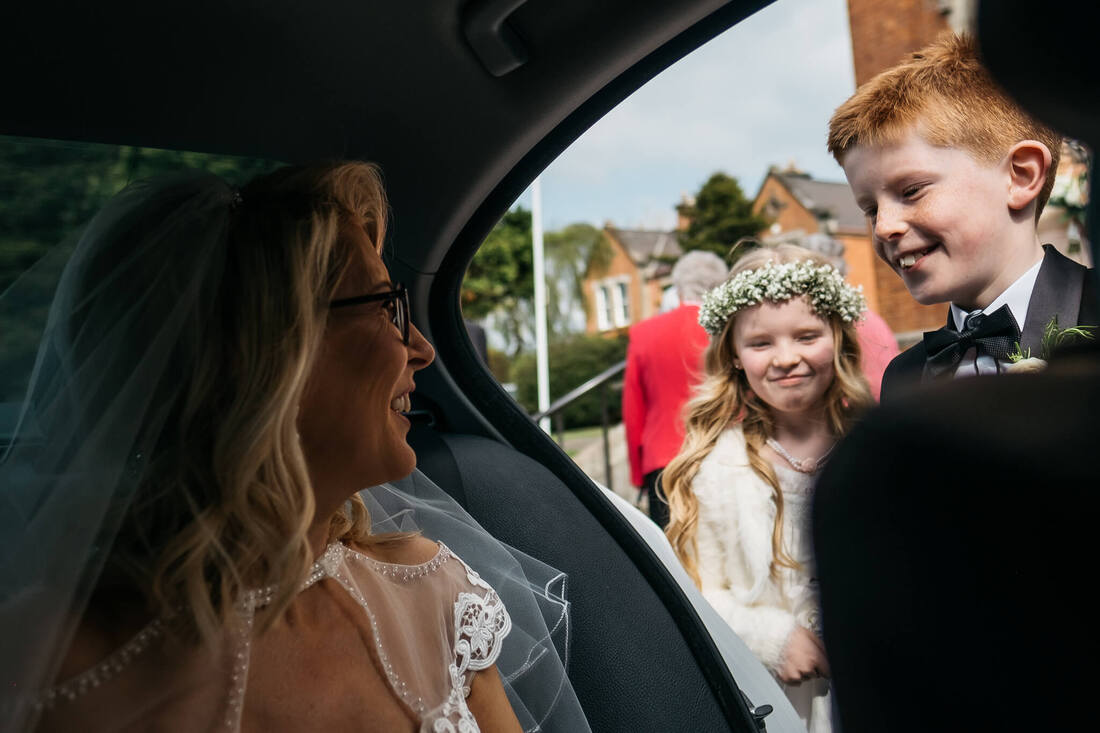 A photograph of pages boy and flower girl and they greet the bride - their mum - as she arrives in the wedding car prior to her Derry wedding