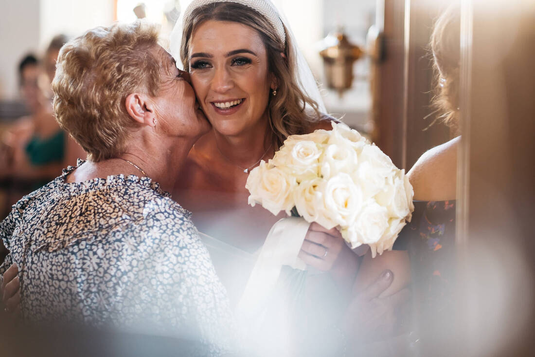 a photograph of a more elderly family member kissing the bride on the cheek at the doors of the chapel following the wedding ceremony