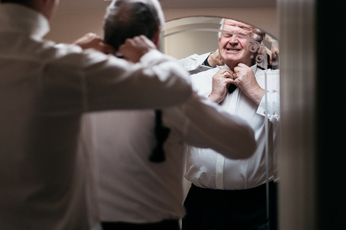 A photogrpah of the father of the groom struggling to close the top button on his shirt on the morning of his son's wedding - his son, the groom is fixing his dad's collar a the same time in Strabane, County Tyrone