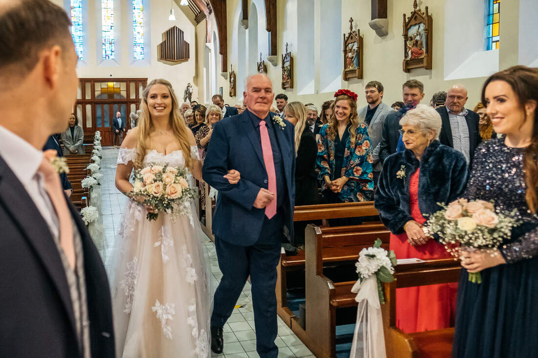 Patrick Duddy Wedding Photography capture of Bride and Groom hand in hand, smiling as they  walk down the aisle after their wedding with friends and family looking on