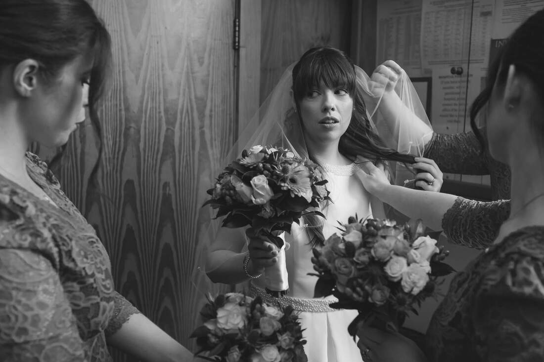 A photograph of a flustered bride as her three bridesmaid make last minute adjustments as they wait in the foyer of the chapel prior the her wedding in Derry