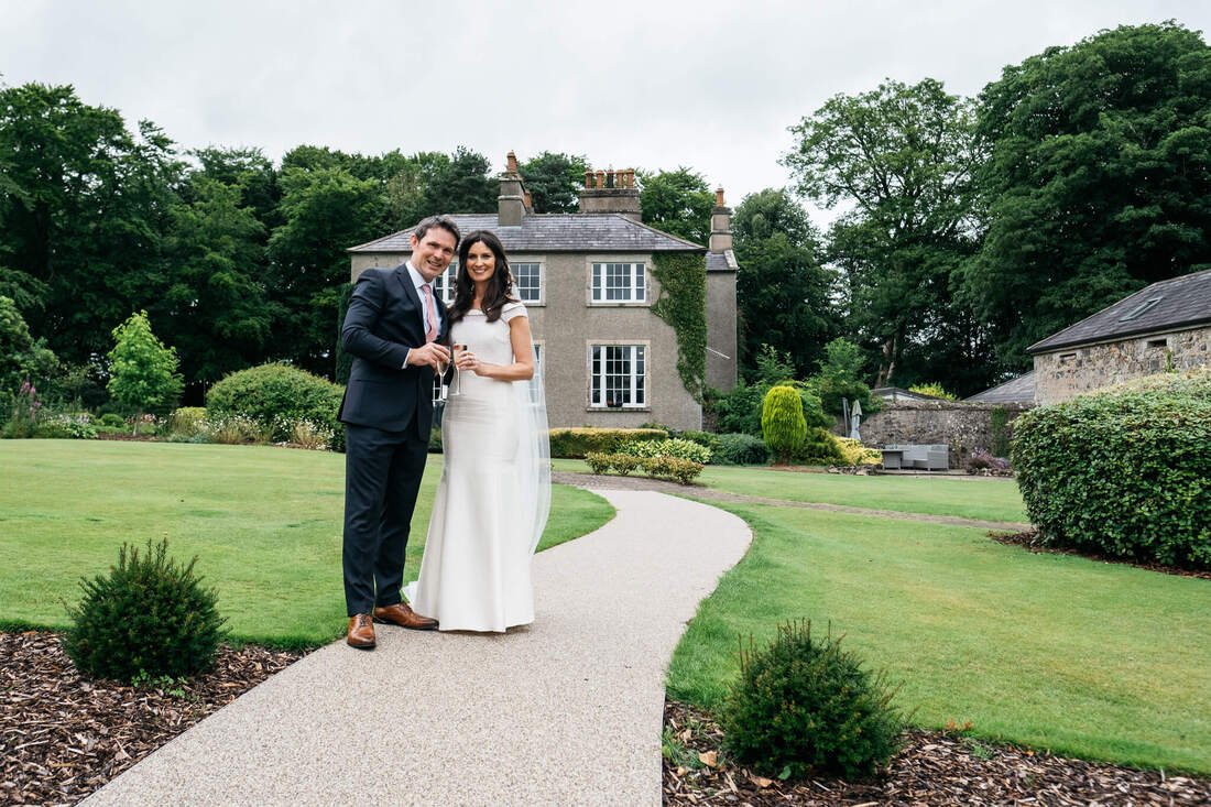 Bride and groom on their wedding days, holding two champagne flutes in the gardens of The Old Rectory, Killyman by Patrick Duddy Photography