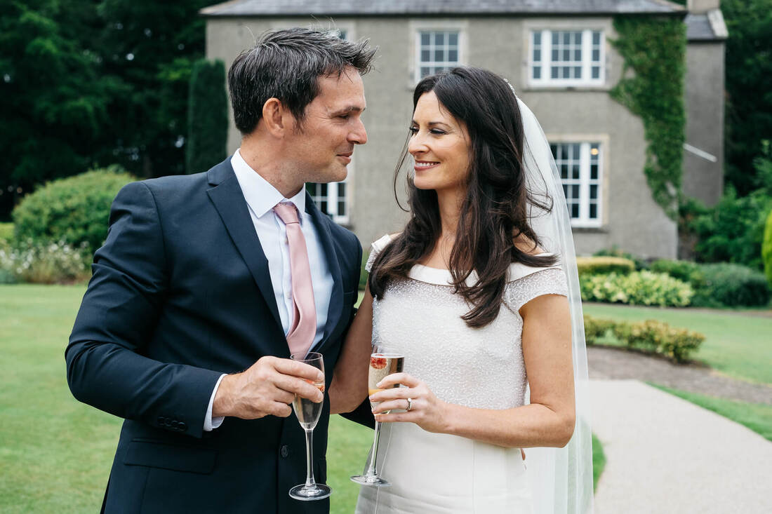 A close up of a Bride and groom facing each other on their wedding days, holding two champagne flutes in the gardens of The Old Rectory, Killyman by Patrick Duddy Photography