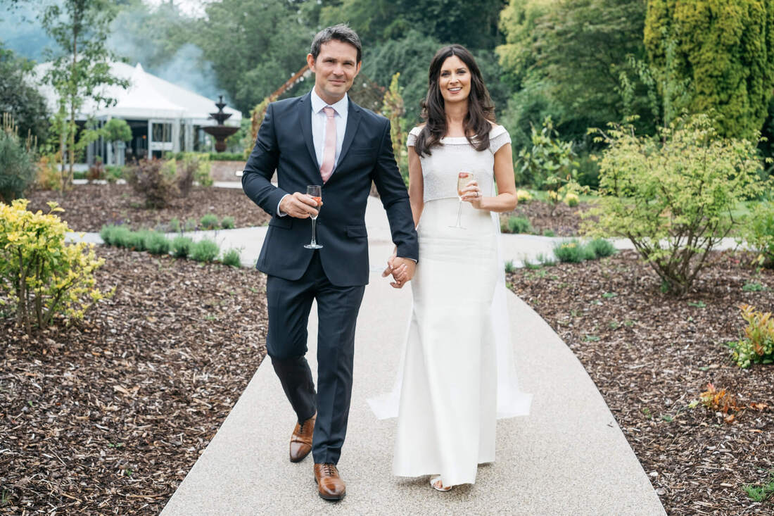 Bride and groom on their wedding days, holding two champagne flutes while walking through the gardens of The Old Rectory, Killyman by Patrick Duddy Photography