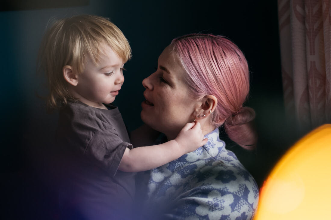A photography of a pink haired Derry Mum holding her new born daughter while her son plays beside them