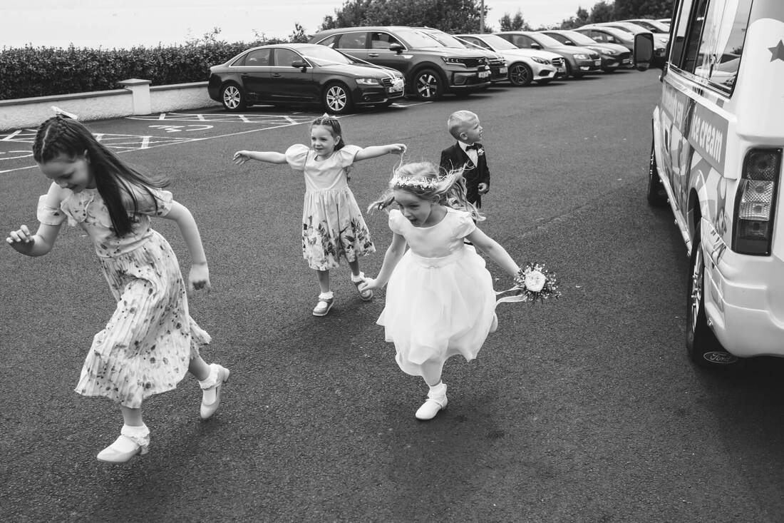 ICE CREAM! Young wedding guest running, full of excitement, to let other guests know there's an ice-cream van outside the church on the day of an Irish Summer Wedding